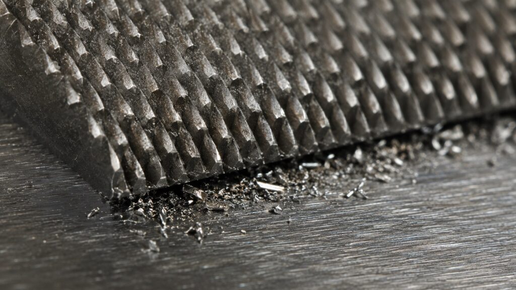 Macro close-up of hardened file teeth cutting mild steel